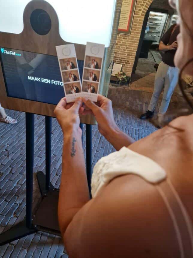 Close-up van een bruid die gepersonaliseerde fotostrips bekijkt die net zijn geprint uit de photobooth. De fotokader bevat het logo van het bruidspaar en maakt de foto's tot een tastbare herinnering aan de bruiloft.