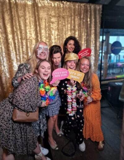 photobooth-trouwfeest-fotoprops Groep vriendinnen met kleurrijke props en feestaccessoires poseert vrolijk voor een photobooth op een trouwfeest. De fotobooth zorgt voor hilarische foto's en veel interactie tijdens de bruiloft.